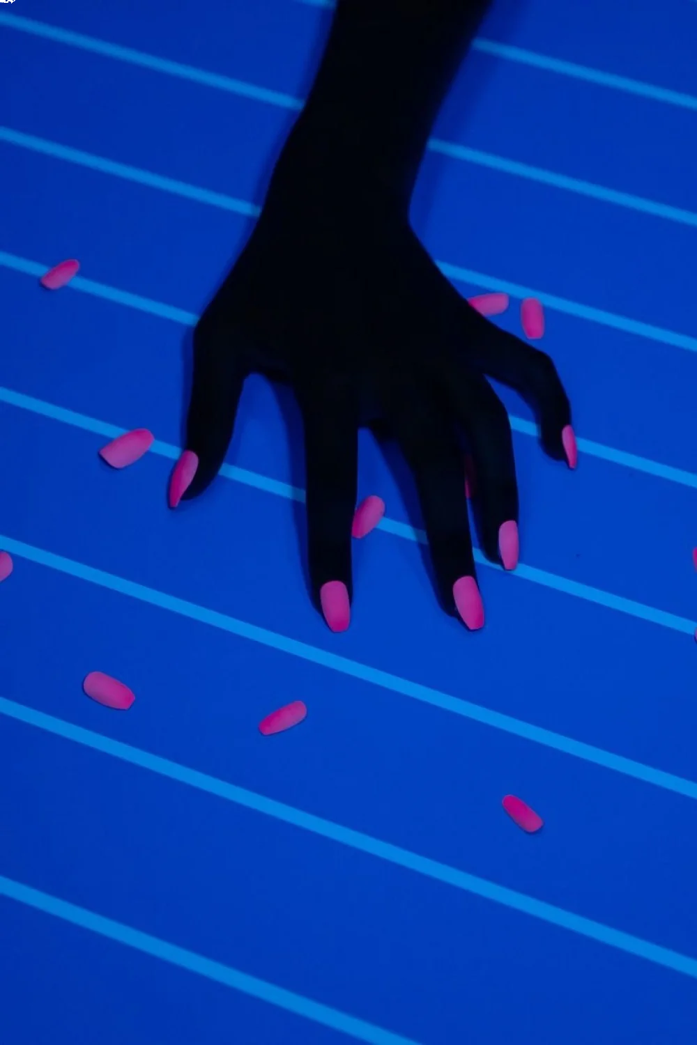 Close-up of summer acrylic nails in neon pink and orange gradient on a blue striped surface with water droplets